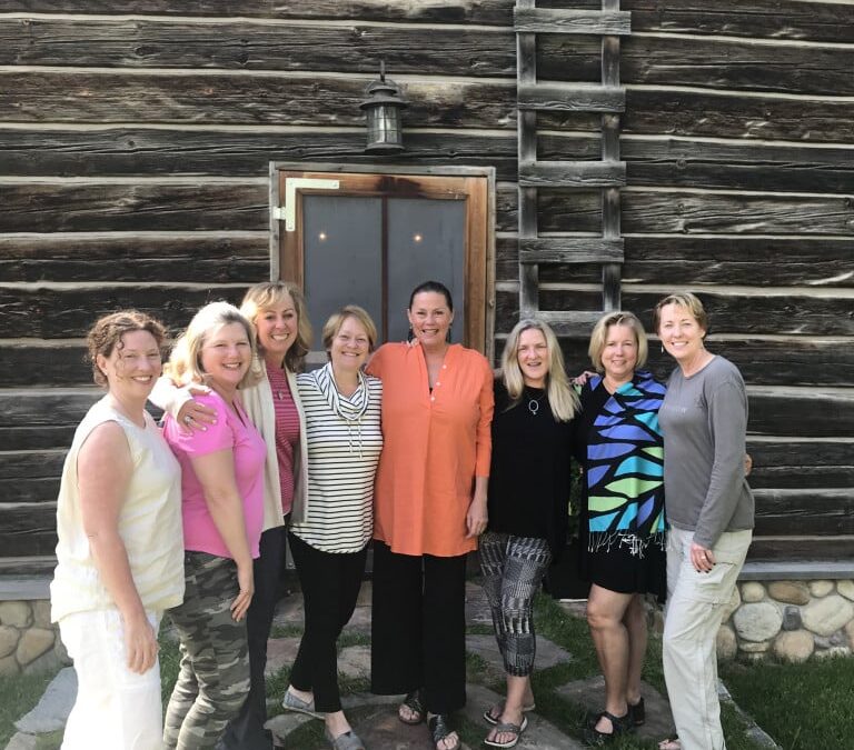 Group of women in front of log building smiling after completing the Haven Writing Program